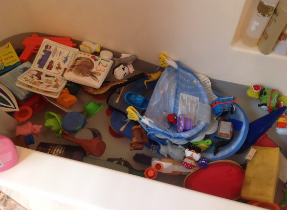 Image of a bathtub filled with water and tons of toddler toys, including books and plastic cups. So many toys that there’s no room basically for a little body.