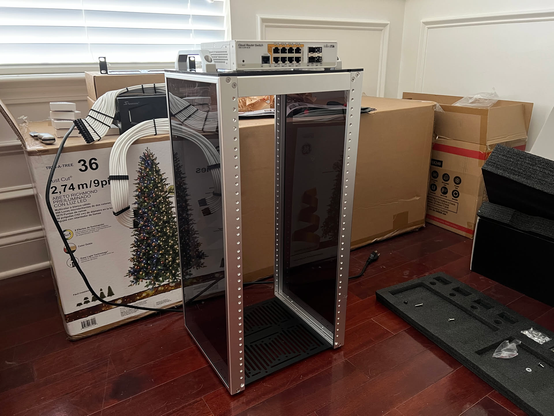 A 12U 10" rack with smoked acrylic sidepanels.  On top is a smol PoE switch made by Mikrotik.