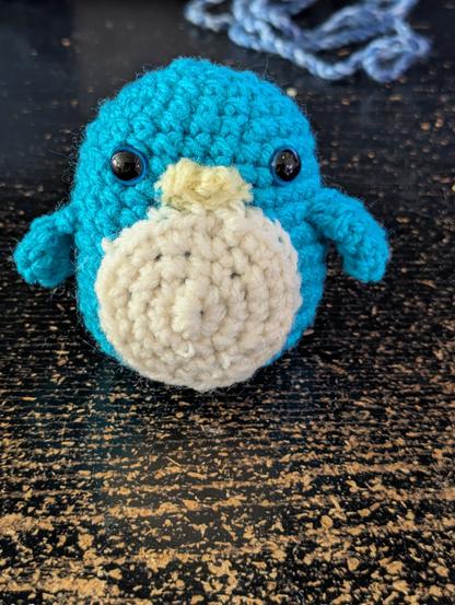 A small blue crocheted penguin. It is very round.