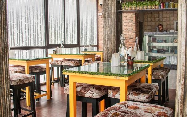 A bright restaurant interior with yellow tables, upholstered stools, and large windows.
