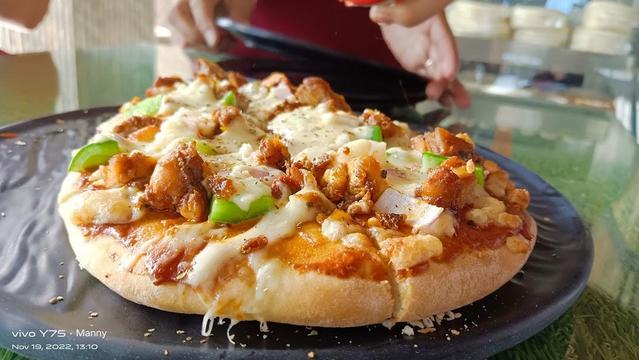 A close-up shot of a chicken pizza with green peppers, onions, and cheese on a black plate.
