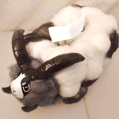 Dubwool, the Sheep Pokemon, in tissue box form. It has a black and white, egg-shaped head with brown horns and fluffy gray wool enveloping its neck. The body is rectangular with white wool and black spots. On top of the body is an opening with a tissue sticking out.