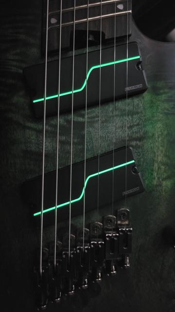 Close up of guitar pickups on a multiscale 7 string guitar. The pickups are Fishman Fluence Modern Stephan Carpenter signatures, which have a glow in the dark strip following the classic Fluence design. The guitar body is green with a burl top, and features lots of nice wood textures and variations. The edge of the body is outlined in purple.