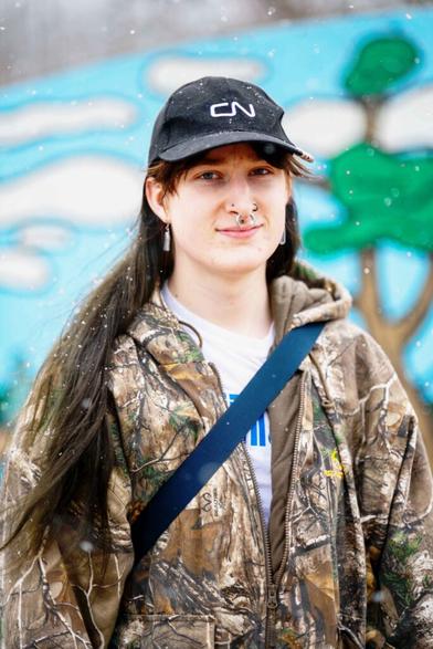 Photo of Willa Coward, wearing a hunter's camo jacket and a black CN rail hat, taken outside in the snow.