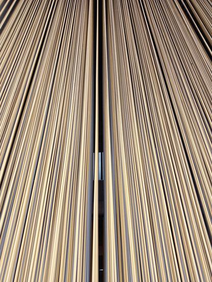 A close up photo of the bars of a kinetic sculpture seen from below. A blue window is visible in the distance behind the sculpture.