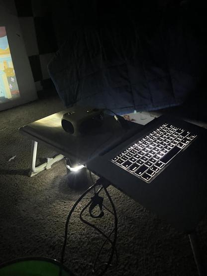 Dimly lit room with a laptop with no screen attached to a small projector on a small stand.