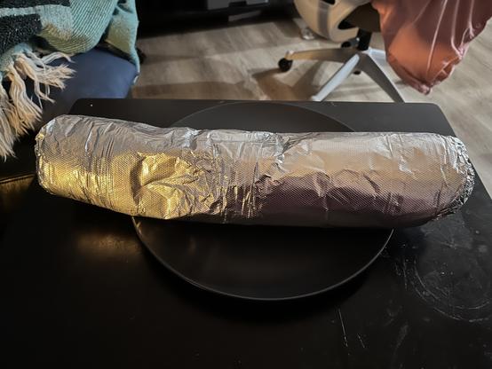 Burrito wrapped in foil that's so long it exceeds the large plate three inches on both sides.