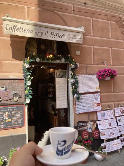 A cafe entrance in Italy. A small coffee cup and saucer are in the foreground. The cafe has a sign that says "Caffetteria Il Bricco".