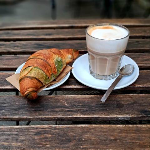 A croissant and a latte on a wooden table.