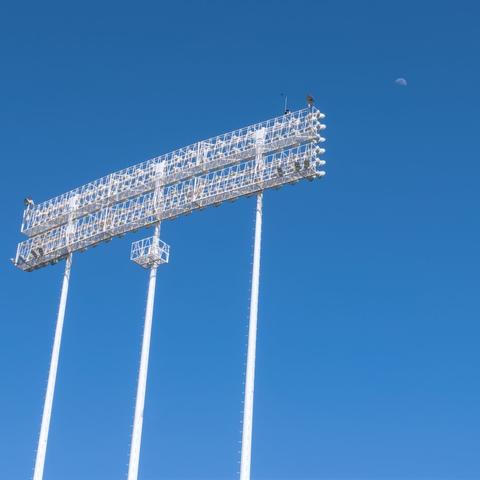 The light gantry from a stadium against a dark blue sky, with the moon in the distance