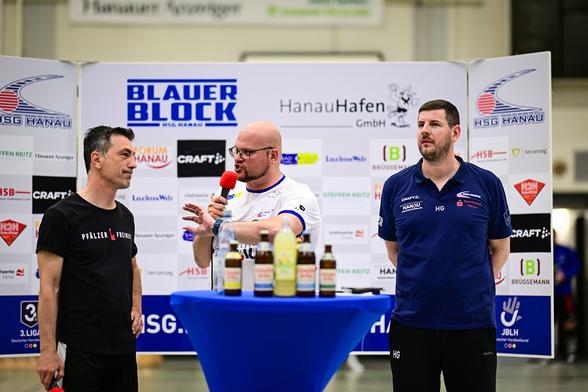 Daniel R. Schmidt führt die Pressekonferenz nach dem Spiel vor einer Sponsorenwand durch. Neben ihm befinden sich die beiden Trainer der TSG Haßloch und der HSG Hanau.