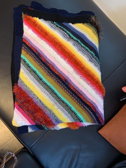 Eine gefaltete gestrickte Decke mit vielen schmalen bunten Streifen aus verschiedenen Garnen