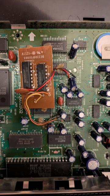 A little brown PCB mounted with a capacitor and two 74series logic ICs mounted on top of a big green MegaCD PCB
