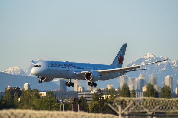 an Air Canada Boeing 787 on short final approach to runway 26L of YVR. its the golden hour, and the sun casts a bright golden light on everything. behind the airplane, the city of Vancouver is visible, with tall snow-capped peaks in the horizon