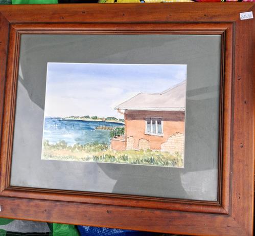 A framed watercolour of a beach scene, with a corner of a little terracotta coloured house in it. There is a wooden jetty too
