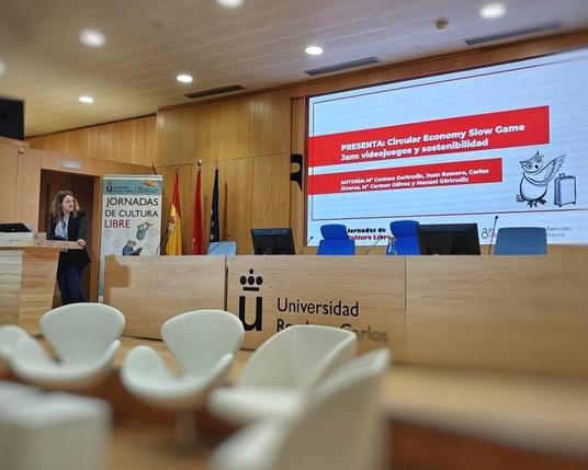 Una mujer presenta frente a una gran pantalla, compartiendo información con la audiencia.