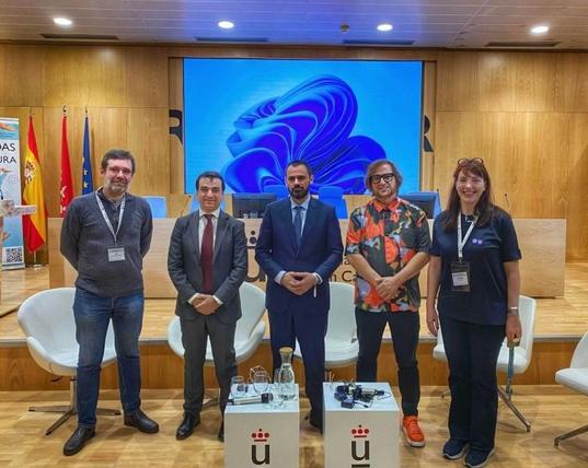 Un conjunto de individuos, equipo de ofilibre y candidatos a rector de la URJC, de pie ante una pantalla.