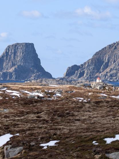 Blue sky, mountains and a white-red lighthouse with burnt grass in the foreground.