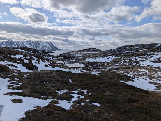Patches of snow over burnt grass and the sea in the background.
Mountains can be seen very far away.