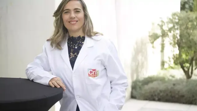 La investigadora Guadalupe Sabio de pie con una bata blanca de laboratorio con el logotipo de la Fundación Cris contra el cáncer.