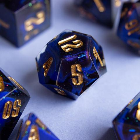 Ein D12 mit goldenen zahlen. Dahinter glitzert es und man sieht einen Farbwirbel aus Ultramarin, Schwarz und colorshifting mica.