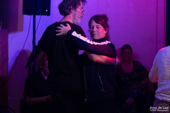 Een foto van twee dansende mensen. De achtergrond is paars door de gekleurde lampen.