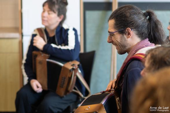 Een foto van twee mensen met een trekharmonica op hun schoot. De ene is een jongen met lang haar in een staart die lacht. De andere ben ik met ook lang haar in een staart en een meer luisterend gezicht.