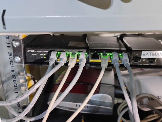 Photo eines Netzwerschrankes mit diversen Blechen, auf einem ein zyxel POE-8+2-port-Switch, beschriftet "BATMAN", darunter eine AVM-Fritzbox 4040