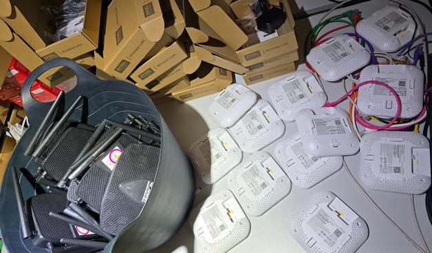 Photo eines Tidches voller Zyxel Accesspoints (NWA50AX), dahinter kartons dieser, links ein Gummi-Futtereimer mit Totolink X5000R Routern)