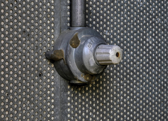 Foto eines alten Drehknopf-Lichtschalters, explosionsgeschützt, auf einer Schalldämm-Wand aus Metall-Lochblech mit Dämm-Material dahinter.