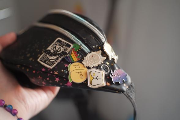 Photo de ma sacoche, il y a des étoiles bleues, violettes et roses et des pin's dont un triceratops bisexuel