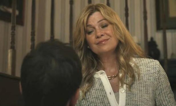 Ellen Pompeo smiles at someone we see from the back. She has a smug expression. Her hair is very long and she wears and expensive looking sweater of brown knit.