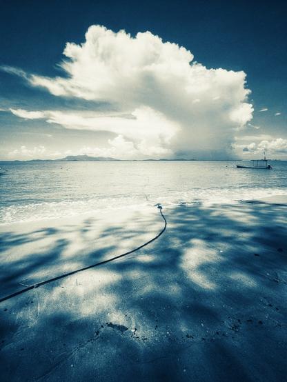a large anvil develops over the ocean on the horizon in a sapphire blue hued beach landscape