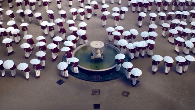 A scene of Conclave overlooking a group of cardinals walking in the rain towards the Sistine Chapel, each holding a white umbrella.