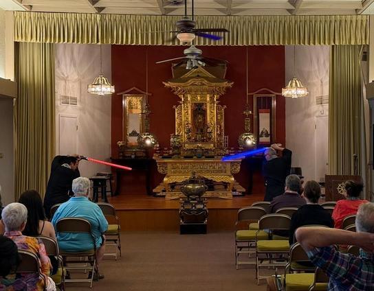 Two monks with lightsabers face off in front of the statue of Amida Buddha at Arizona Buddhist Temple.