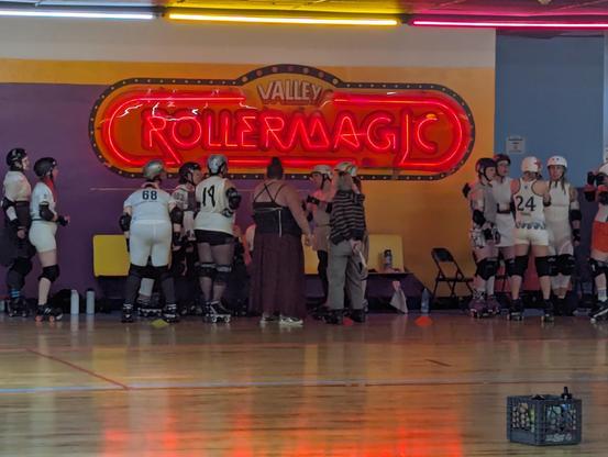 Roller derby referees stand in front of a sign saying "RollerMagic."