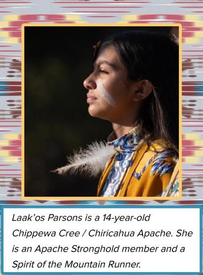 Photograph of a young Cree woman in yellow clothing with blue and white patterns, a feather and white face paint. Laak’os Parsons is a 14 year old Chippewa Cree/ Chiricahua Apache. She is an Apache Stronghold member and a Spirit of the Mountain Runner.