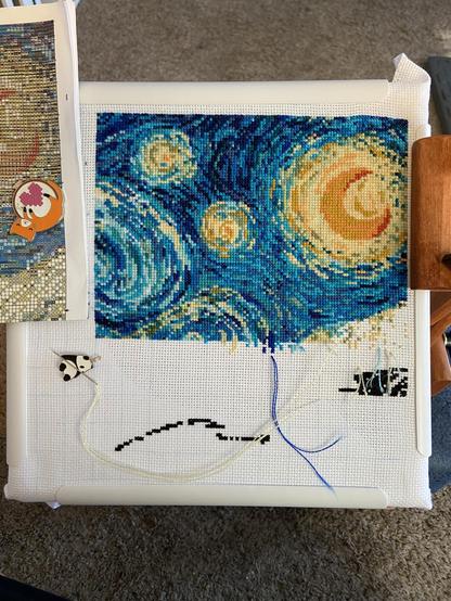 A cross stitch in progress in the likeness of starry night by Van Gogh. It’s in shades of blue and yellow threads