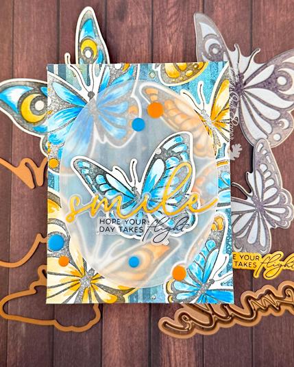 A greeting card with big butterflies watercolored in blue and orange tones. The focal point is a blue butterfly in the center of the card. The greetings sit across it. The main greeting reads "smile" and the subsentiment says "Hope your day takes flight."
