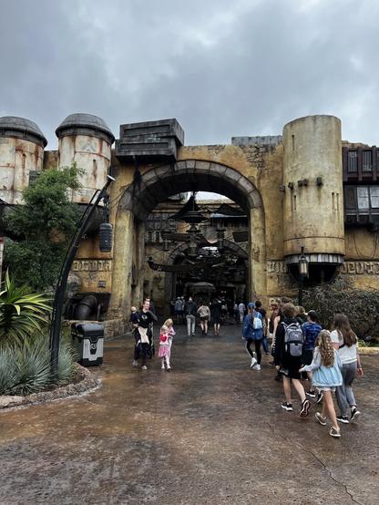 People are walking towards a rustic, science fiction-themed entrance of Black Spire Outpost on the Planet Batuu in Disneyland, California.