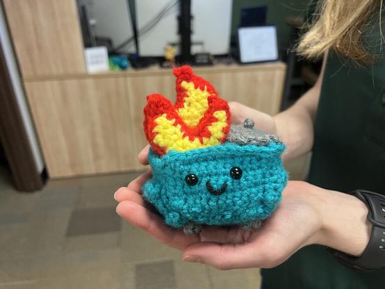 “A crocheted dumpster fire with a happy little face, being held in the palm of someone’s hand”