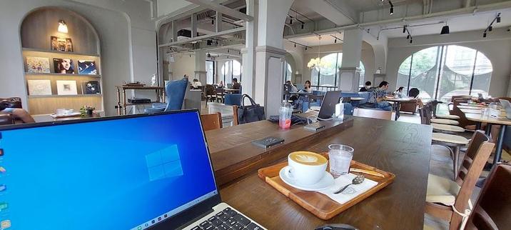 A cafe scene with a laptop, coffee, and other people working.