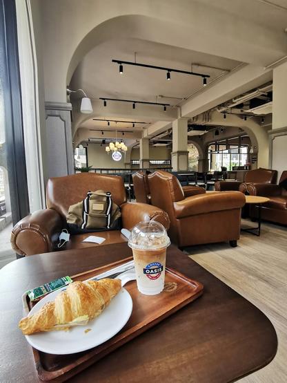 A croissant and coffee on a wooden tray in a cozy cafe.
