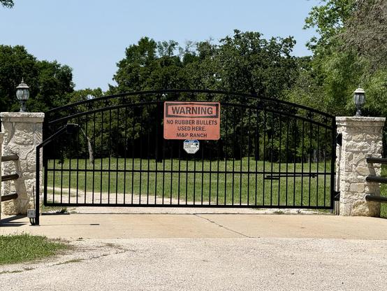 A gate with a big orange sign in the center reading "Warning / No rubber bullets used here / M&P Ranch"