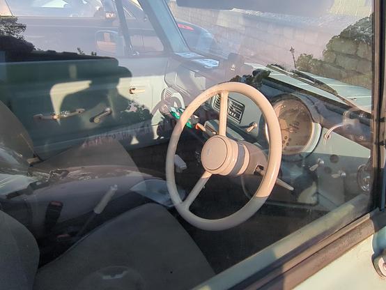 The interior of a Nissan Pao, a small 3-door hatchback reminiscent of a Citroen H-van. The dashboard, pillars and door tops are all in the same light blue paint as the exterior but it's wearing its years quite well. The dashboard features a large central speedometer and white toggle switches. The two-spoke steering wheel is worn, with a shiny plastic finish in a sort of peachy beige colour. Nice.
