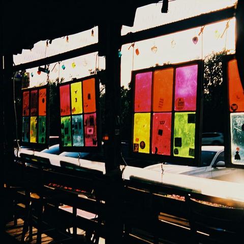 Photograph of backlit, brightly colored windowpanes hanging over an outdoor bartop.
Strong halation visible from the overexposed sky.