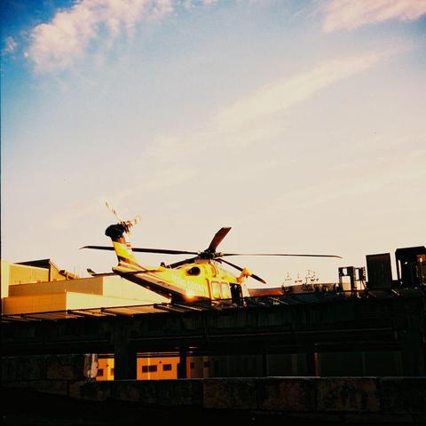 Photograph of a helicopter on a helipad. 
The scene is brightly lit and strong halation is visible around the helicopter and surrounding buildings.