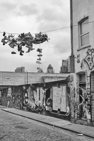 Schwarzweiß Foto mit Schuhe die an einer Leine über einer Straße hängen; black and white photo showing shoes hanging over a street