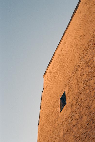 Façade orangée, ciel bleu. Une fenêtre semble cacher un secret derrière quelques barreaux.