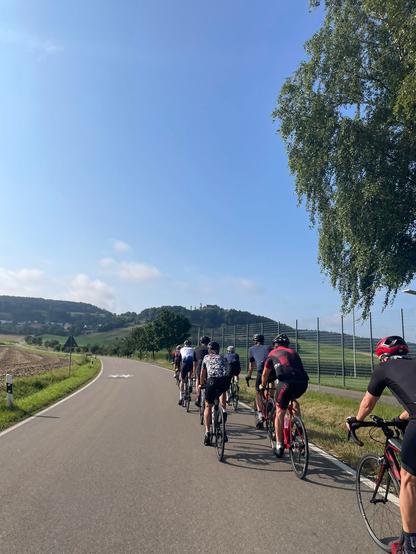 In der Ferne eine Burg. Davor eine Gruppe Radfahrer:innen vor einem Anstieg.
